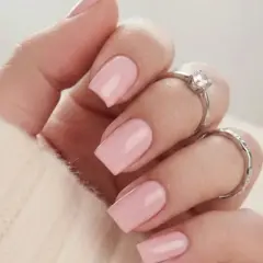 En hand med naglar målade i mjukt nagellack rosa, prydd med två silverringar.