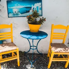 Zwei gelbe Stühle und ein blauer Tisch mit Blumentopf. Ein Bild mit Meerblick hängt an der Wand. Hier sind die Kos Geheimtipps für dein nächstes Foto!