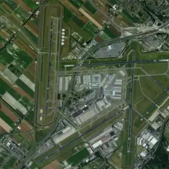 Widok z lotu ptaka na lotnisko Schiphol w Amsterdamie, otoczone polami i drogami.