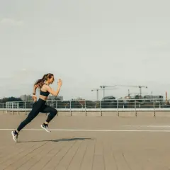 Kobieta w sportowym stroju biegnie, pokonując dystans 5 km. W tle widać miejską panoramę z dźwigami budowlanymi.