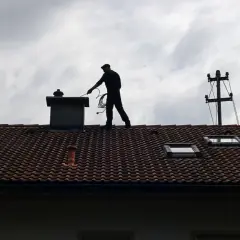 Kominiarz na dachu przygotowuje się do pracy. Zastanawiasz się, ile kosztuje szlamowanie komina?