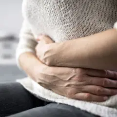 Dłonie obejmujące brzuch, sugerujące ból lub dyskomfort. Może to być objaw problemów żołądkowych, takich jak te, które łagodzi tiorfan.