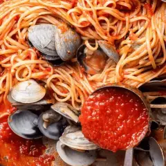 Spaghetti alle vongole, un plat de pâtes aux palourdes et sauce tomate, servi dans une poêle avec une louche de sauce.