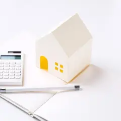 Maison en papier, calculatrice et stylo sur un carnet ouvert, symbolisant les **PTZ travaux soi-même**.