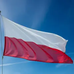Polska flaga powiewa na maszcie na tle błękitnego nieba.