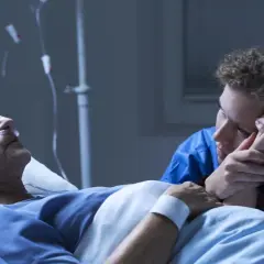 Chora kobieta w łóżku szpitalnym, podłączona do aparatury, trzyma za rękę bliską osobę. Czy leczenie paliatywne to koniec?