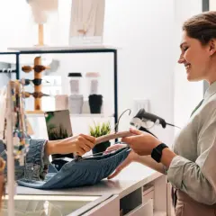 Klientka dokonuje zwrot towaru w sklepie stacjonarnym. Sprzedawczyni uśmiecha się, przyjmując ubranie na wieszaku.