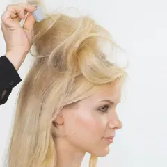 Blonde Frau mit voluminösen Brigitte Bardot Haaren, die von einer Hand mit einem Kamm gestylt werden.