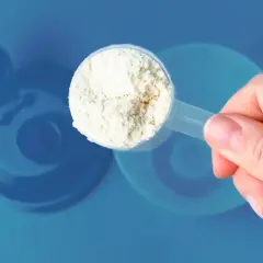 Una mano sostiene una cuchara con polvo blanco, ¿cuanta creatina tomar? Fondo azul con silueta de batidora.
