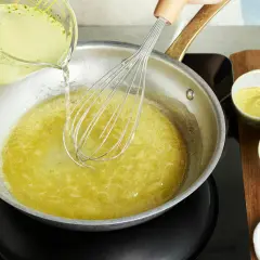 Flüssigkeit wird in eine Pfanne mit einem Schneebesen gegossen, um eine cremige vegane Hollandaise zuzubereiten.