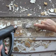 Un décapeur thermique avec réglage de température est utilisé pour ramollir la vieille peinture avant de la gratter.