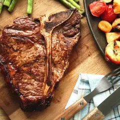 Une côte de bœuf juteuse, accompagnée d'asperges et de tomates grillées, prête à être dégustée.