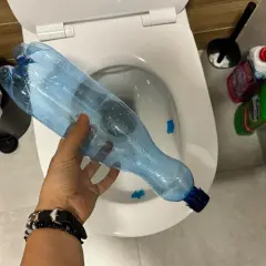 Ręka trzyma plastikową butelkę nad toaletą, pokazując, jak odetkać toaletę bez przepychaczki.