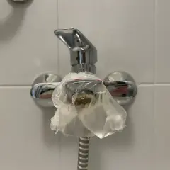 Kran prysznicowy owinięty folią, bo w bloku brak ciepłej wody. Krople zimnej wody spływają po opakowaniu.
