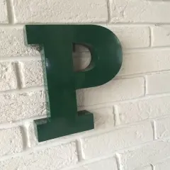 Une lettre murale verte en forme de P est fixée sur un mur de briques blanches.