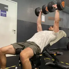 Un homme fait un exercice pectoraux avec des haltères sur un banc incliné dans une salle de sport.