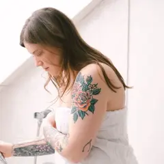 Kobieta w ręczniku z kolorowym tatuażem róży na ramieniu.