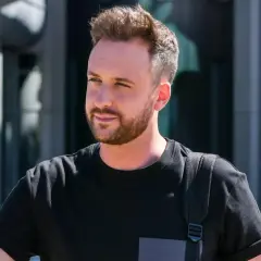 Aleksander Sikora w czarnej koszulce z plecakiem, na tle budynku.