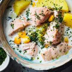 Łosoś w śmietanowym sosie z ziemniakami i kukurydzą, posypany koperkiem. Danie wygląda apetycznie, choć norwegia ceny w restauracjach mogą być wysokie.