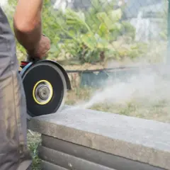 Mann schneidet mit Winkelschleifer eine Betonplatte. Staub wirbelt auf.