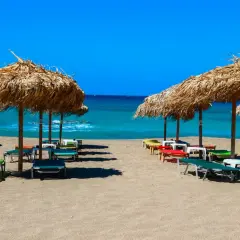 Słomiane parasole i leżaki na piaszczystej plaży Falasarna, z turkusowym morzem w tle.