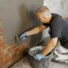 Mann trägt Mörtel auf Ziegelwand auf. Informiert sich über Schleierinjektion Kosten für Feuchtigkeitsschutz.