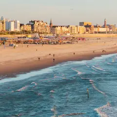 Ein sonniger Tag am **niederlande strand** mit Wellen, Sand und einer Stadtkulisse im Hintergrund.
