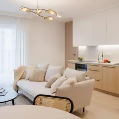 Jasne, przytulne mieszkanie w stylu japandi z kremową kanapą, drewnianymi meblami kuchennymi i minimalistycznym oświetleniem.
