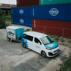 Biały bus z przyczepą, oznakowany logo "Linia", stoi obok kontenerów. To może być szkolenie, gdzie poznasz prawo jazdy b+e koszt.