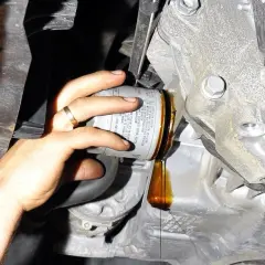 Wymiana oleju i filtrów w samochodzie: ręka odkręca stary filtr, z którego kapie olej.
