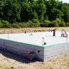 Fundament płyty betonowej z instalacją hydrauliczną i rurami, w otoczeniu zieleni.