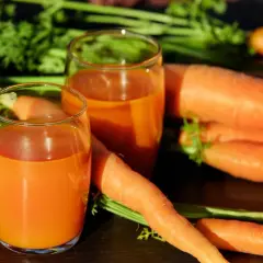 Frischer Karottensaft in Gläsern, umgeben von ganzen Karotten. Ein tolles Beispiel für vitamin a welche lebensmittel.