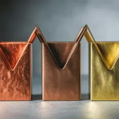 Trois porte-stylos aux formes géométriques, en laiton et cuivre, aux textures variées.