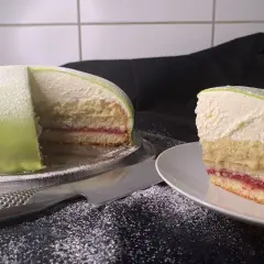 En vacker prinsesstårta med grön marsipan och ett lager sylt. En bit är upplagd på en tallrik.