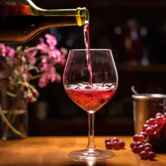 Czerwone wino nalewane do kieliszka, obok kiść winogron. To może być najmocniejsze wino domowe, które rozgrzeje serce.