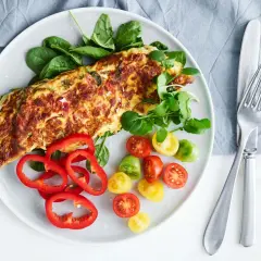 En gyllene, nyttig omelett serverad med färska grönsaker som spenat, körsbärstomater och paprika. En perfekt start på dagen!