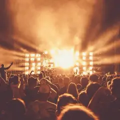 Tłum ludzi na Sunrise Festival Poland, z rękami w górze, w blasku świateł scenicznych i dymu.
