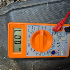 Pomarańczowy multimetr z wyświetlaczem pokazującym 0.07, podłączony czerwonym i czarnym przewodem.