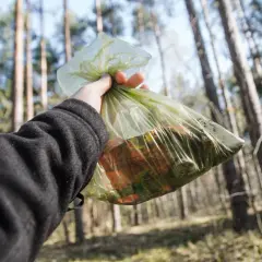 Ręka trzyma worek ze śmieciami w lesie. Zasady "leave no trace" to dbanie o przyrodę.