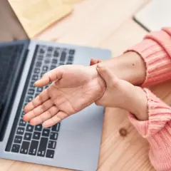 Dłoń masuje nadgarstek przy laptopie, szukając domowych sposobów leczenia cieśni nadgarstka.