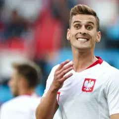 Piłkarz reprezentacji Polski z szerokim uśmiechem, jakby cieszył się z każdego wieku sukcesu. Biała koszulka z godłem orła.