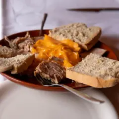 Plato de lomo en manteca con pan rústico y una salsa cremosa de queso.