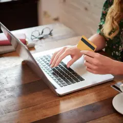 Kobieta z kartą płatniczą na laptopie, szukająca pożyczki dla każdego bez odmowy. Kawa obok.