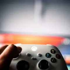 Dłoń trzyma biały kontroler Xbox, gotowa do gry. Wiedza to potęga, podobne gry wymagają strategii i refleksu.