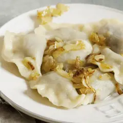Pyszne pierogi z kapustą i skwarkami, ułożone na białym talerzu, kuszą swoim domowym wyglądem.