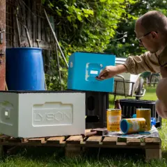 Mężczyzna maluje nowoczesne ule na niebiesko. Obok stoi biały ul z logo Lyson.