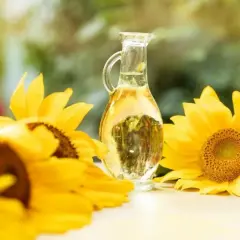 Słonecznikowy olej (helianthus annuus seed oil) w karafce, otoczony przez piękne, żółte słoneczniki.