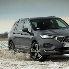Szary Seat Tarraco SUV przemierza błotniste, zaśnieżone pole, wzbijając chmury brudu.