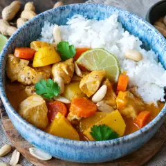 Ein köstlicher Massaman Curry mit Hühnchen, Kartoffeln, Karotten und Erdnüssen, serviert mit Reis und Limettenspalten.