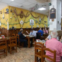 Gente comiendo en la abacería el arrecife, decorada con motivos marineros. Mesas de madera y paredes amarillas con redes y barcos.